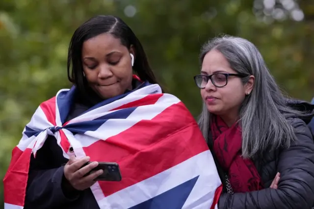 People look at a phone as they await the procession, on the day of the state funeral and burial of Britain's Queen Elizabeth, on The Mall in London on 19 September 2022