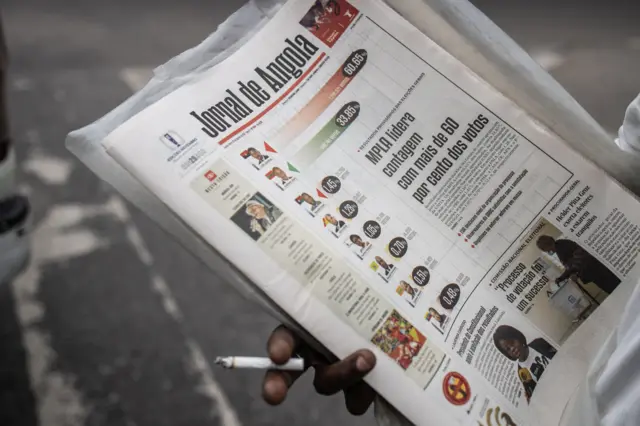 A newspaper vendor smokes a cigarette whilst holding Jornal de Angola newspapers with the election results on the front page in Luanda on August 25, 2022.