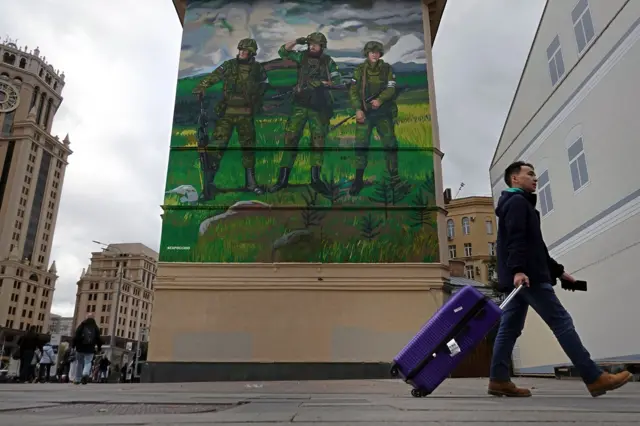 A man walks in front an apartment block decorated with a mural in support of Russia's army 'special military operation' in Ukraine