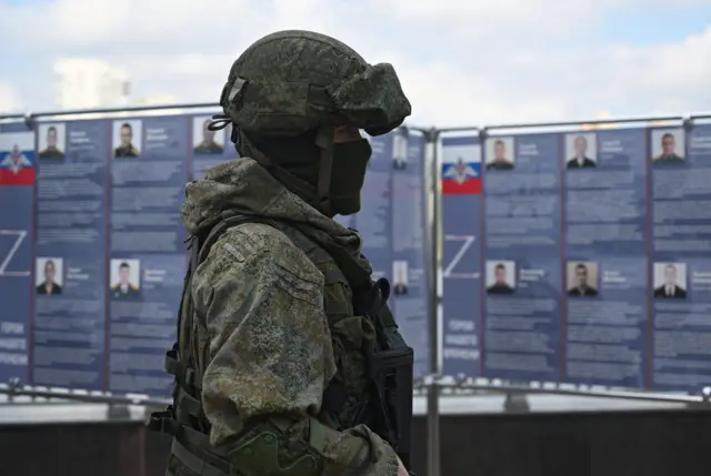 A Russian service member stands next to a mobile recruitment center for military service