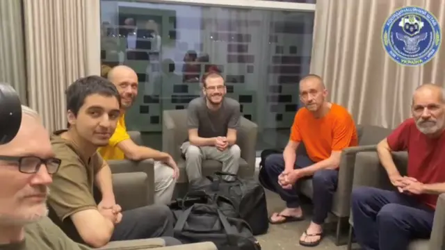 The exchanged prisoners of war - including British national Shaun Pinner in orange - sit after disembarking from their flight to Saudi Arabia, before heading back to their respective countries