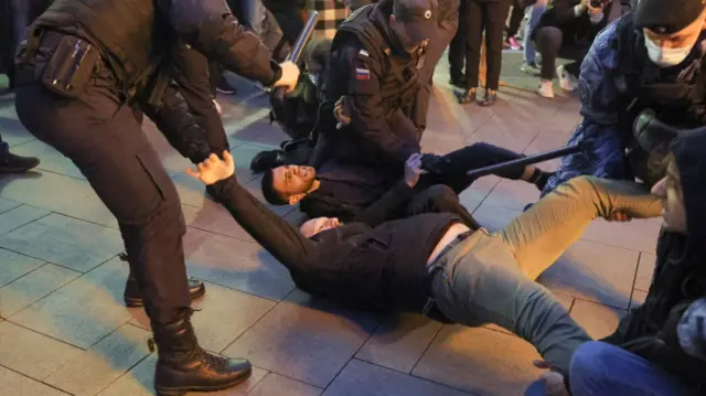 Two men are detained on the ground during the unsanctioned rally, with officers carrying them away by the legs and arms