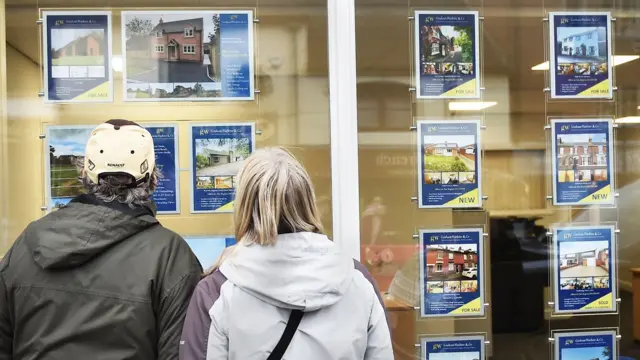 A man and woman look at an estate agent's window display