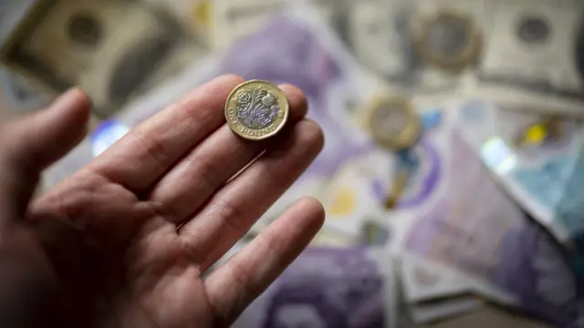 Someone holds a pound coin above a background of bank notes