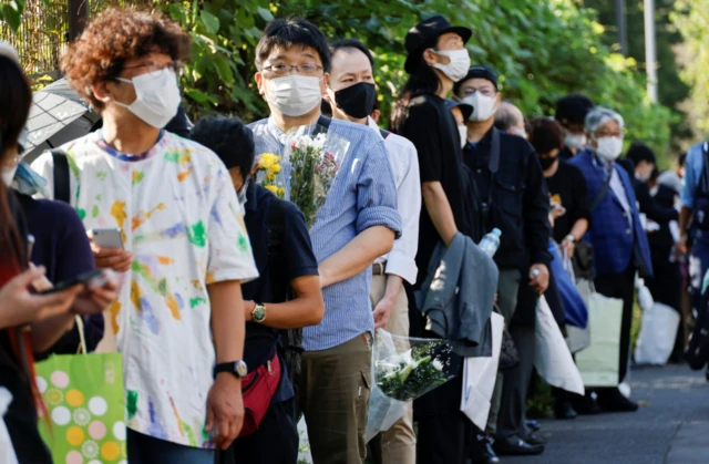 A queue of mourners outside the funeral venue holding flowers and other tributes