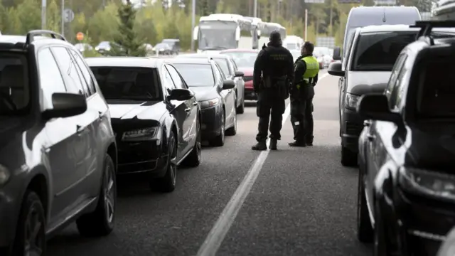 Finnish border guards stand among Russian vehicles at a checkpoint