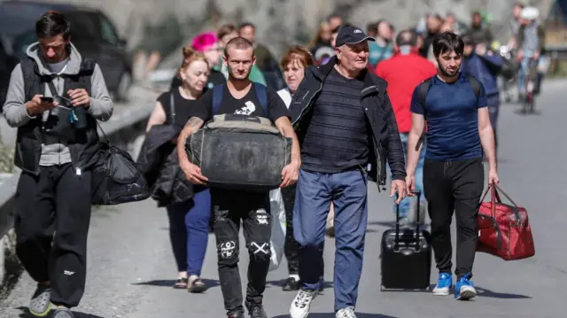 Russian men and women with their luggage walk along a road after passing through customs at the Georgia-Russia border checkpoint of Verkhnii Lars, Georgia, 27 September 2022.