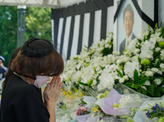 A woman dressed in black and wearing a veil prays at an altar for Mr Abe