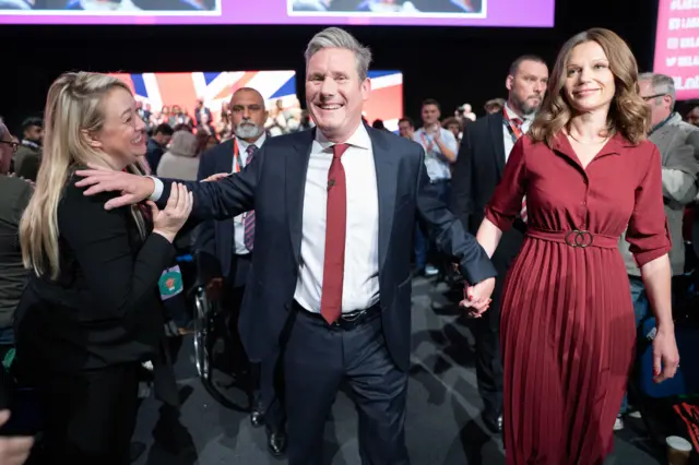 Starmer walks out of the hall after his speech grinning hand-in-hand with his wife