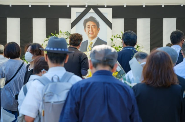 People stand in front of a tribute site with Mr Abe's photo on it