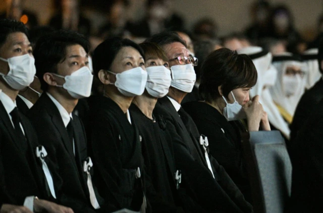 Akie Abe cries while mourners seated next to her watch a video tribute to her late husband