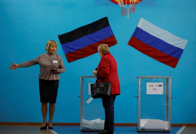 A member of an electoral commission shows the way to a voter at a polling station during a referendum on the joining of the self-proclaimed Donetsk People's Republic