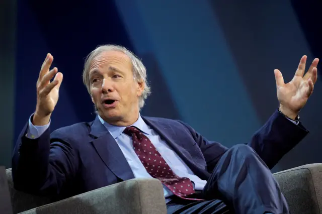 Investor Ray Dalio gestures with his hands while sat in an armchair at an onstage event