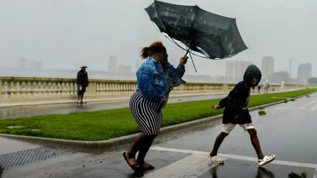 A woman wrestles with her umbrella as she feels the effects of Hurricane Ian