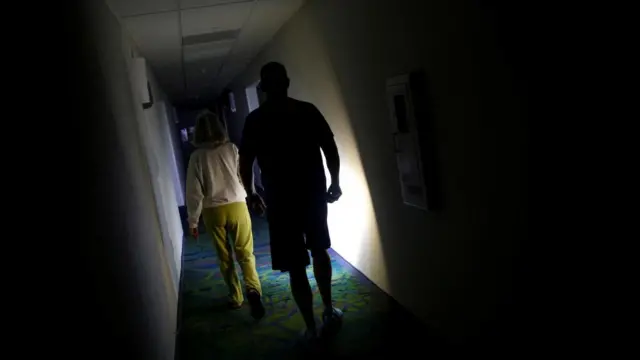 A couple using a torch in an unlit hallway