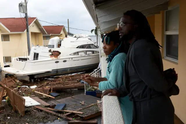 Frankie Romulus (L) and Kendrick Romulus stand outside of their apartment next to a boat that floated into their apartment complex when Hurricane Ian passed through the area on September 29, 2022 in Fort Myers, Florida