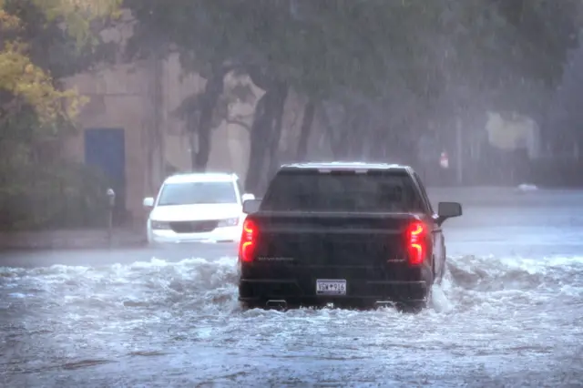 Two vehicles drive on a flooded street