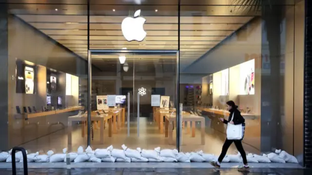 A woman walks past a row of sandbags in front of a shuttered Apple Store