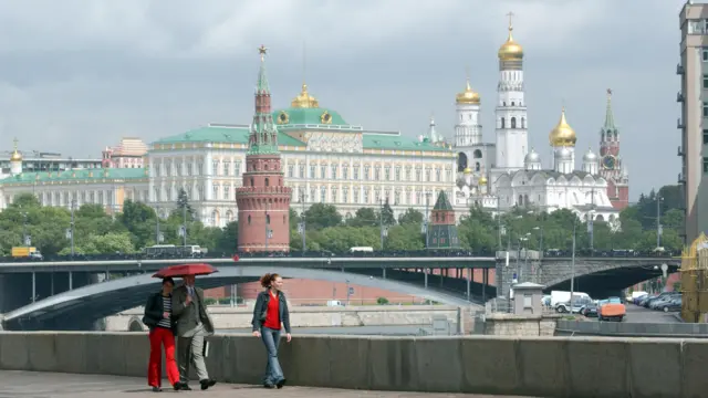 People walk past the towers on the walls of the Kremlin, with the Grand Kremlin Palace visible behind