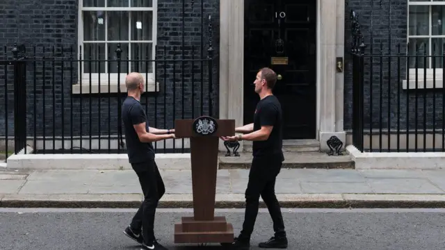 Two men carry a lectern outside Downing Street