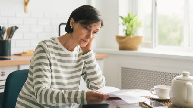 A woman looks at an energy bill while sitting at a kitchen table