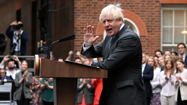 Outgoing British Prime Minister Boris Johnson holds his hand up in what looks like a waving gesture as he makes his final speech in Downing St