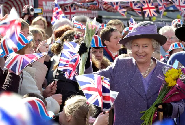 Queen Elizabeth II is surrounded by a huge crowd in London, giving her bouquets of flowers. March 2003