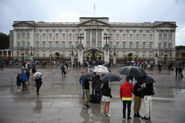 Tourists stand in the rain outside Buckingham Palace in London