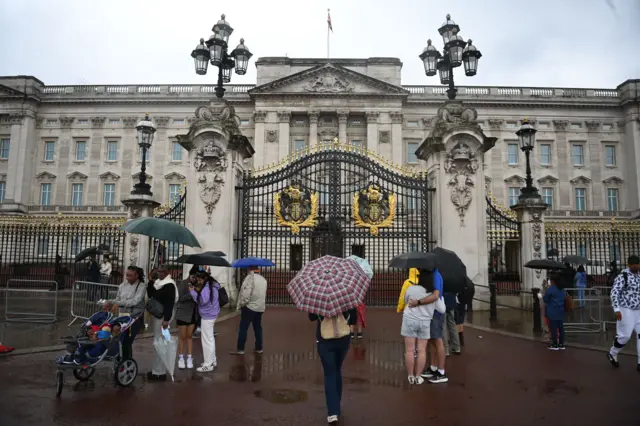 Tourists stand in the rain outside Buckingham Palace in London