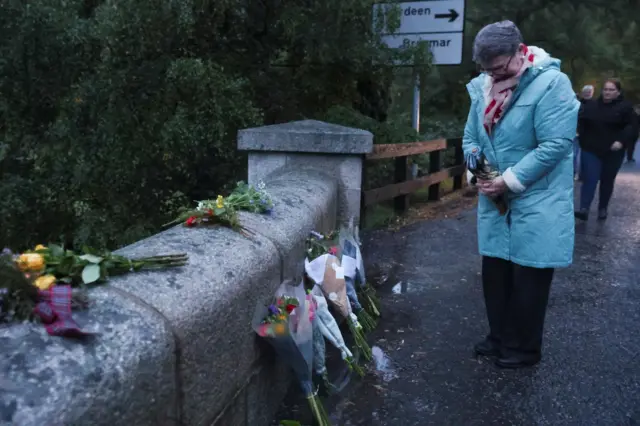 A woman bows her her next to flowers which have been place by an entrance to Balmoral Castle, Scotland