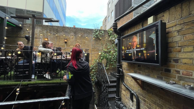 At the Bunch of Grapes pub in London Bridge a security guard and people tune in to watch King Charles III's speech