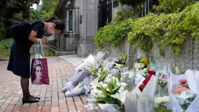 A woman bows her head before a pile of flowers left outside the British embassy in Tokyo