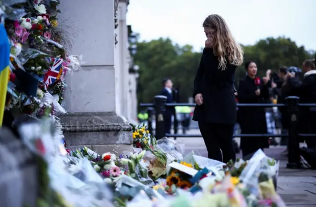 A woman stands among floral tributes at Buckingham Palace