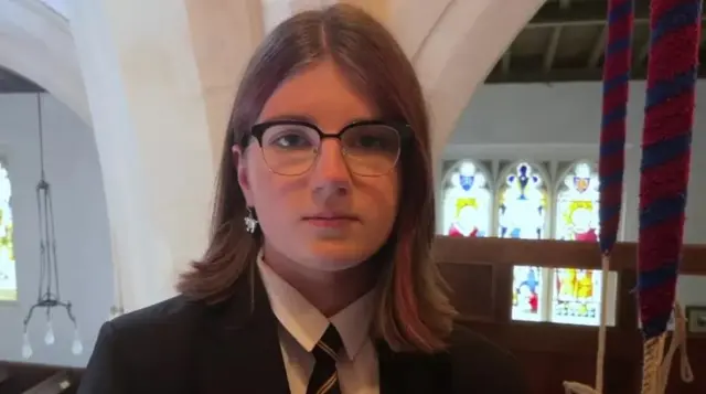 Abi stands in her school uniform next to the bells in the church