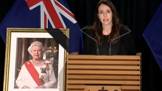 Jacinda Ardern speaks at a press conference with a picture of Queen Elizabeth II