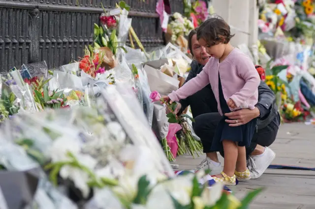 A woman and a child lays a single pink rose by the railings at Buckingham Palace