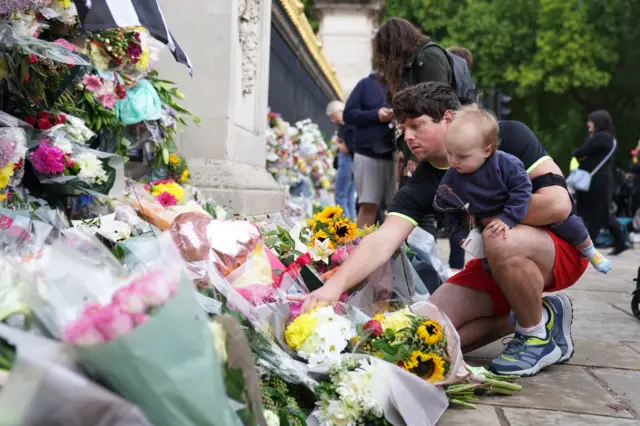 A man with a young child lays flowers outside Buckingham Palace