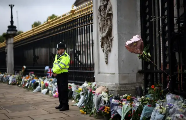 A police officer stands among flowers outside Buckingham Palace