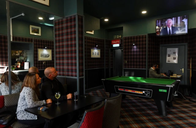 A couple watch King Charles III's address while in the Balmoral Bar, Ballatar