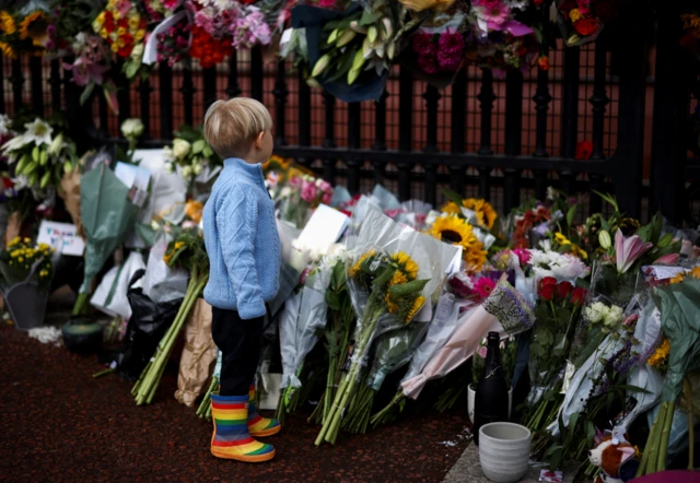 A child stands near the floral tributes placed at Buckingham Palace