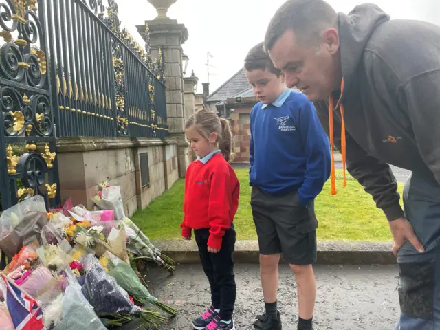 Robin Campbell with his son James and daughter Anna, observe the floral tributes laid at the gates of Hillsborough Castle in County Down, following the death of Queen Elizabeth II on Thursday.