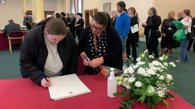 Abbie and her mother Maria Willis, signing a book of condolence at Cardiff City Hall, with a queue of people behind