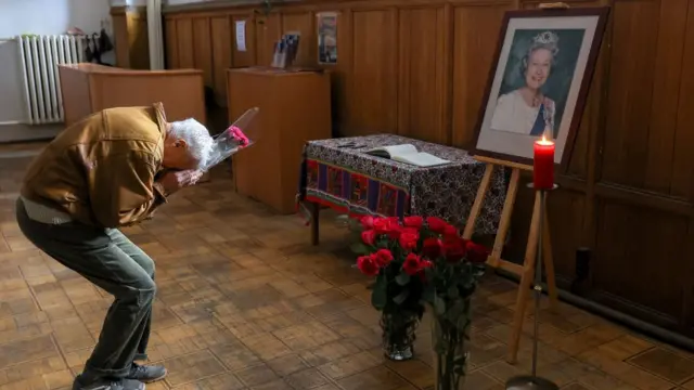 A man carrying flowers before a portrait of the Queen in a Moscow Anglican church