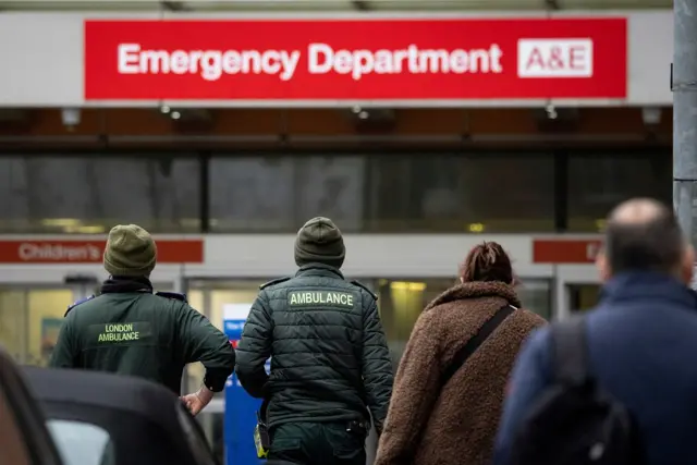 Ambulance workers and people walk into a hospital's A&E department