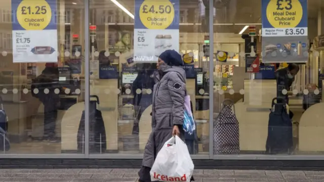 A woman carrying a shopping bag walks past a Tesco supermarket