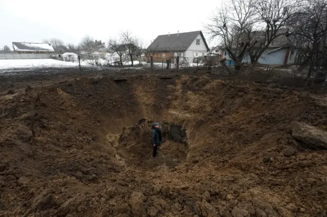 A man stands inside a crater left by a Russian missile in the village of Kopyliv, Kyiv region