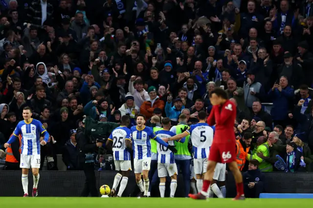 Liverpool's Alexander-Arnold covers his face in anger as Brighton celebrate their second goal.