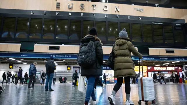 Passengers look at the information board at Euston Station in London