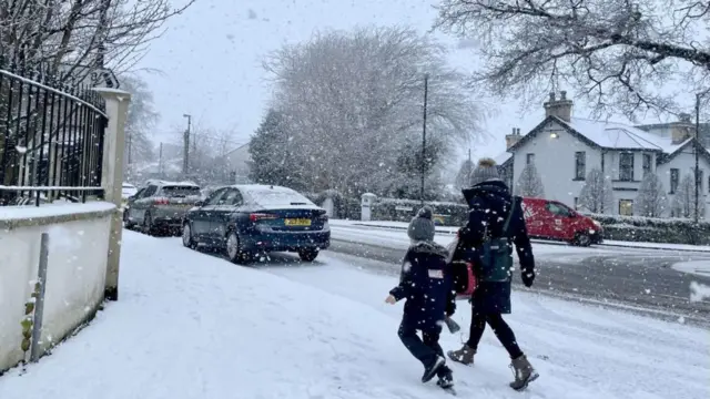 A woman and a child walk through falling snow in Eglinton in Londonderry