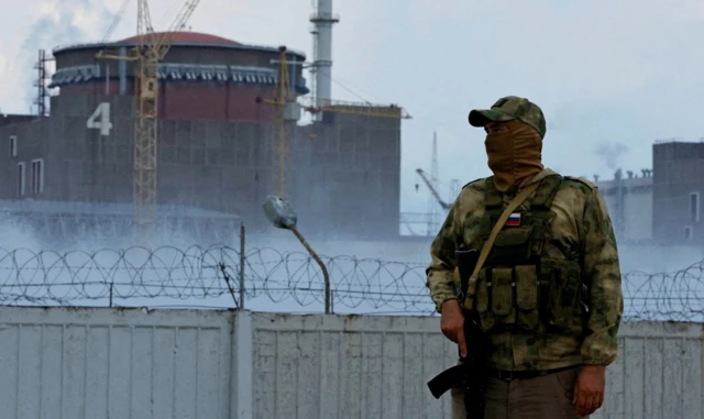 A serviceman with a Russian flag on his uniform stands guard near the Zaporizhzhia Nuclear Power Plant